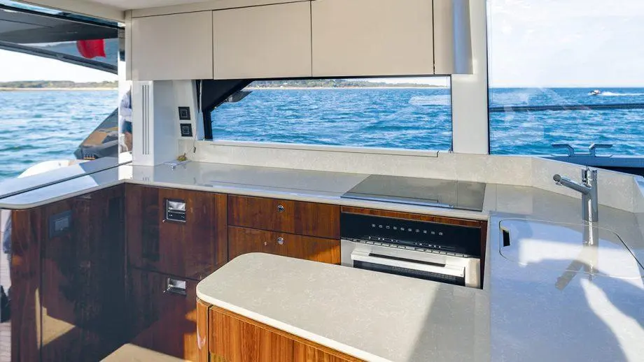 Modern boat kitchen with wooden cabinets, a marble countertop, and a view of the ocean through large windows.